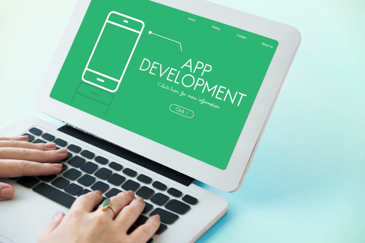 Persona escribiendo en una laptop que muestra el diseño de una aplicación móvil