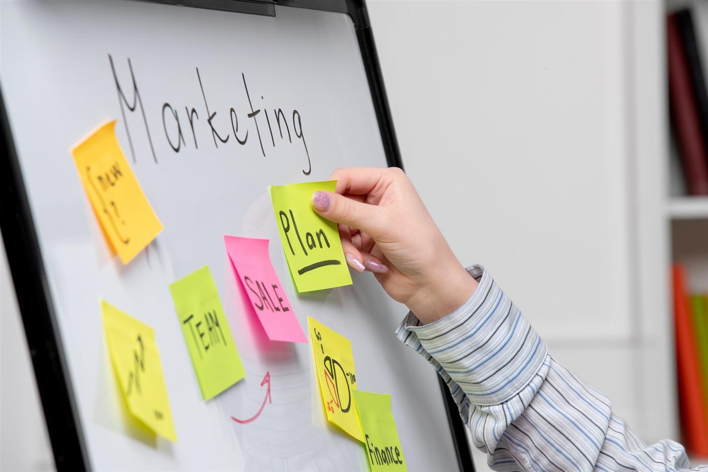 Mano pegando notas adhesivas en un pizarrón de planeación de marketing